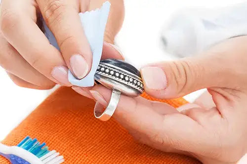 A close-up of hands cleaning a silver ring with a white cloth over an orange towel.