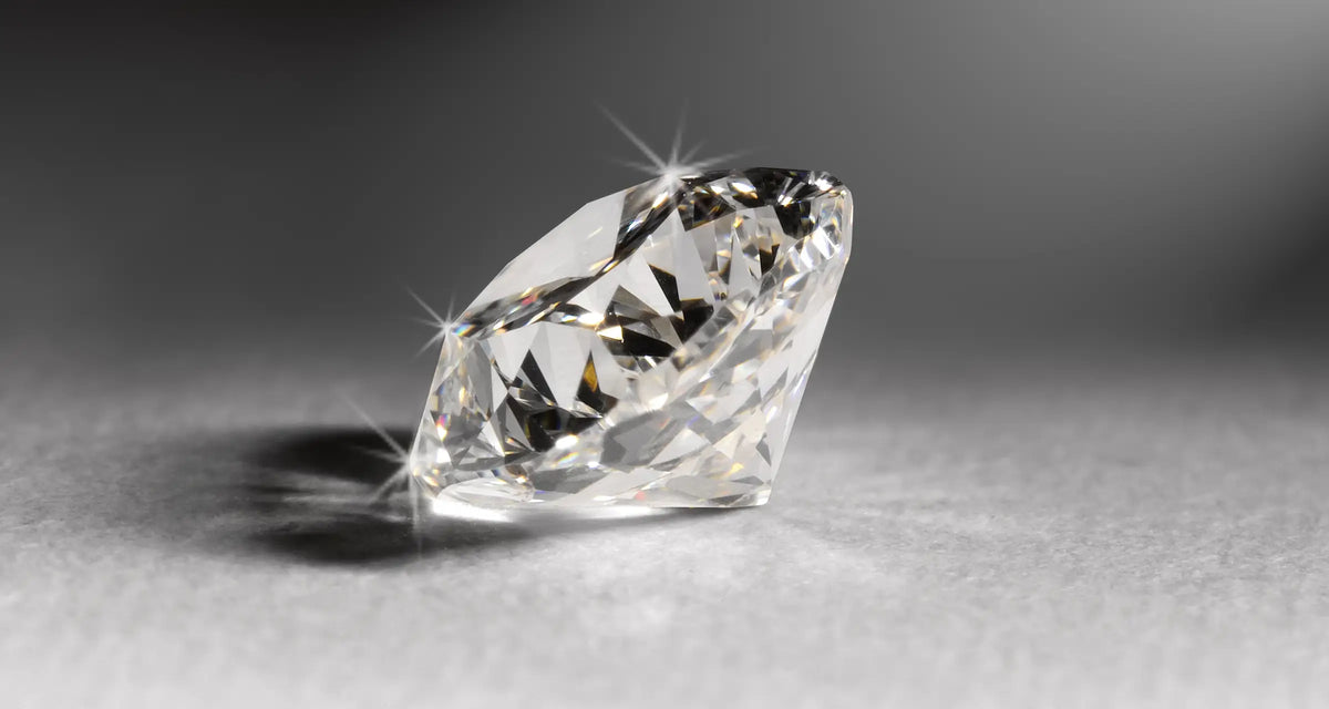A single brilliant-cut diamond gemstone shown in a close-up studio shot on a smooth gray surface with a soft gradient background.