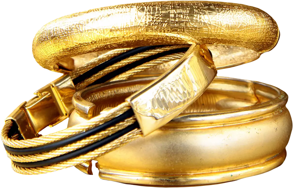A stack of gold-toned jewelry pieces, including a thick textured gold bangle, a gold-toned cable bracelet with black inlay, and a polished gold-toned ring, isolated on a white background.