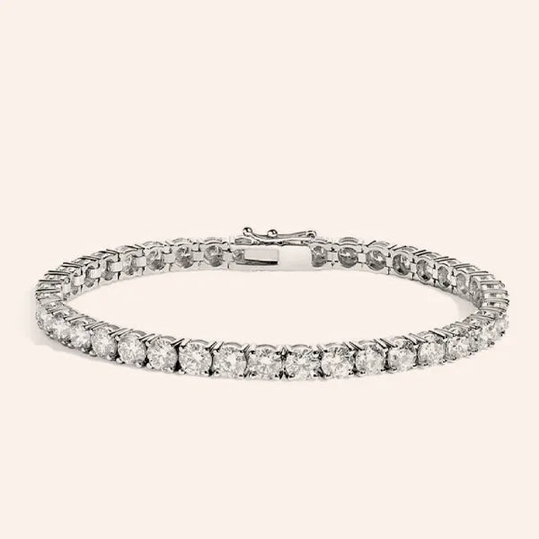 A silver tennis bracelet with a continuous row of round-cut clear gemstones, shown against a solid pale pink background.
