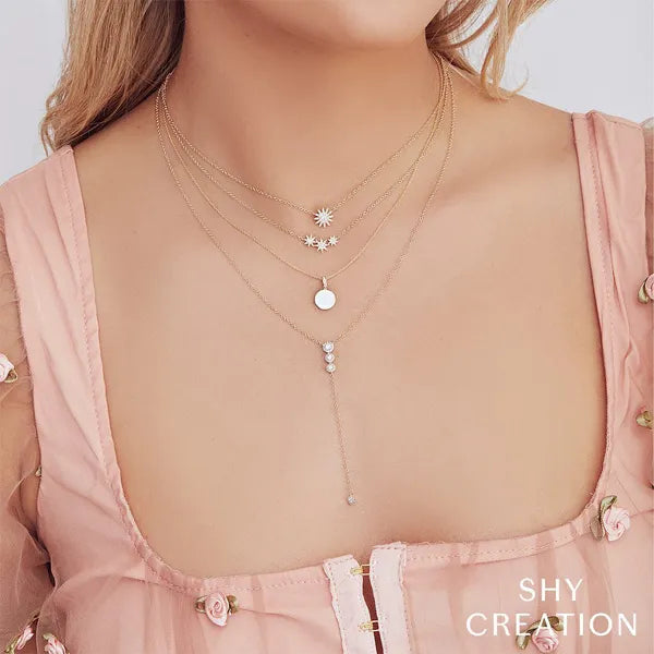 Necklace with small pendants on a person wearing a pink top, with 'SHY CREATION' branding.