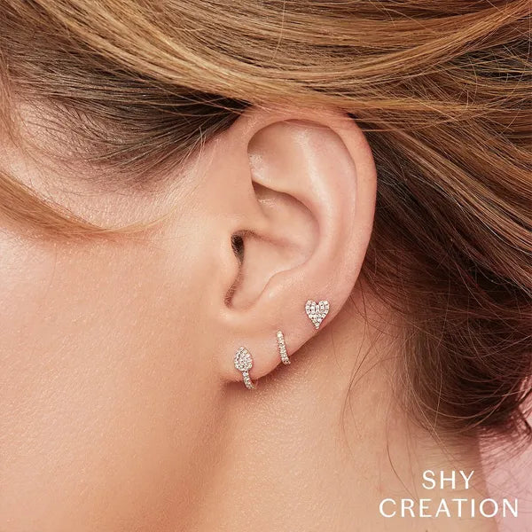 Close-up of an ear wearing three pairs of earrings with 'SHY CREATION' branding.