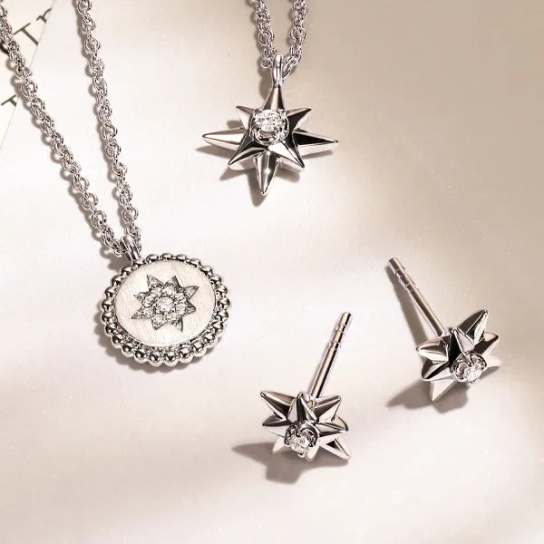Silver-toned jewelry set featuring a starburst pendant necklace, a circular starburst medallion pendant, two matching starburst stud earrings, and a chain, arranged on a light beige background.