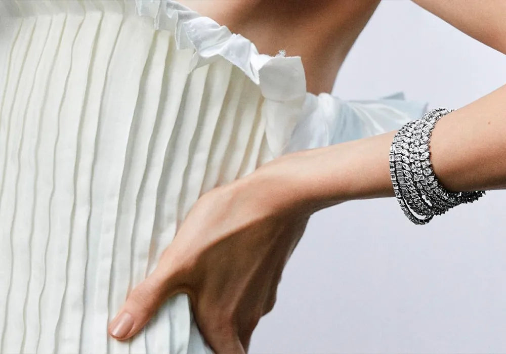 A close-up of a model wearing a multi-strand silver bracelet with clear stones, paired with a white pleated top.