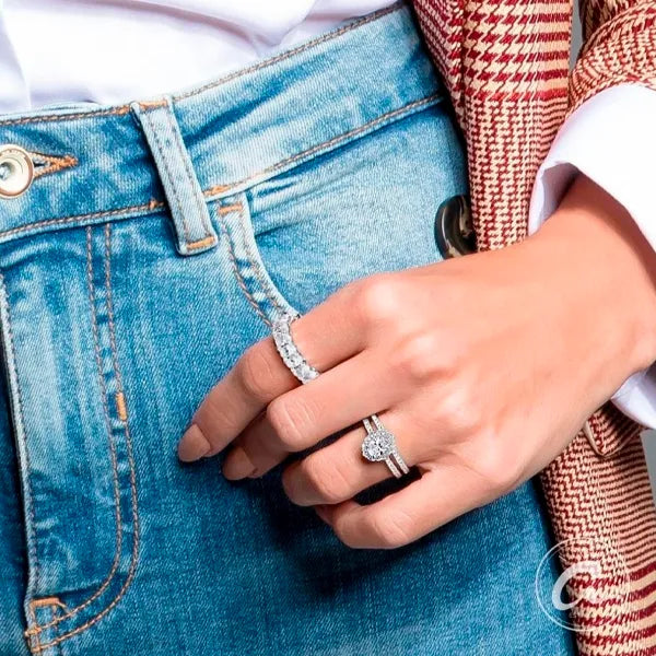 A close-up lifestyle shot of a person wearing a silver heart-shaped ring and a matching silver band with a diamond-encrusted eternity ring, styled with blue jeans and a red-and-white houndstooth blazer.