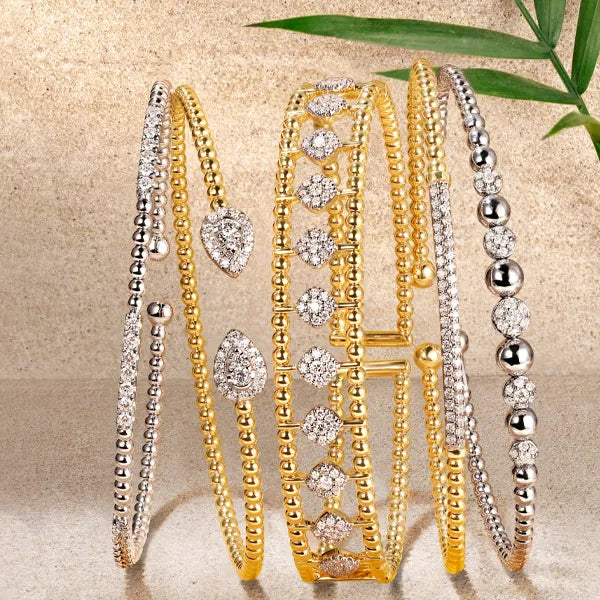 Six gold and silver beaded bangles with clear crystal embellishments, arranged vertically on a textured beige background with a green leaf in the corner.