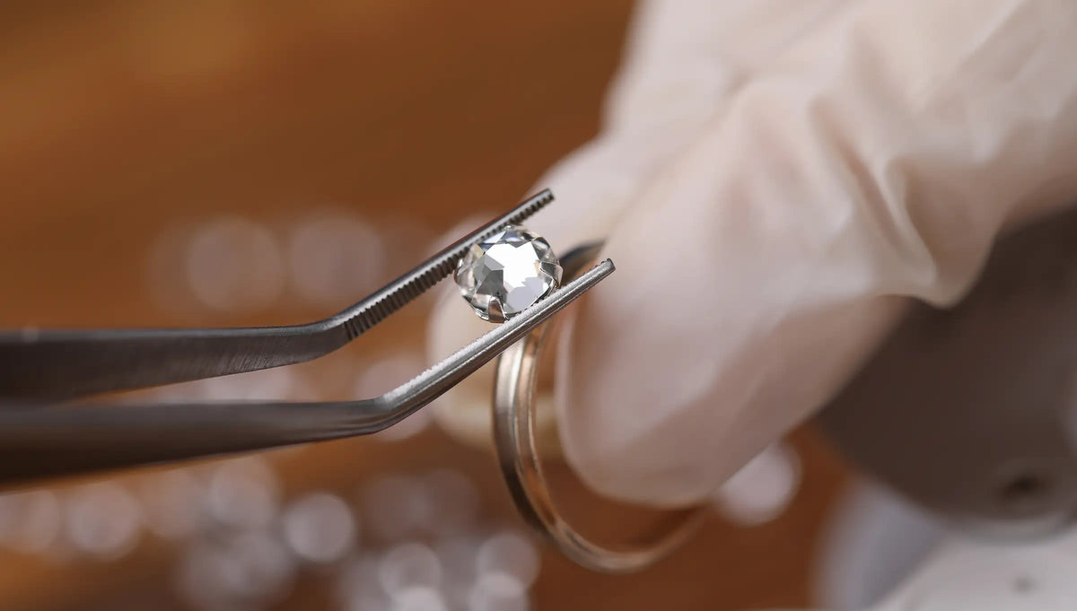 Person wearing gloves holding a diamond with tweezers against a blurred background