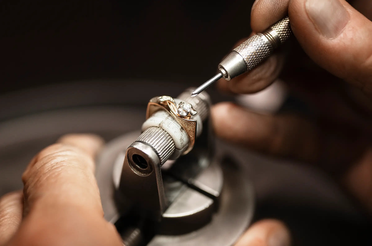 Close-up of a jeweler's hands using a diamond-setting tool on a ring holder under bright focused light.