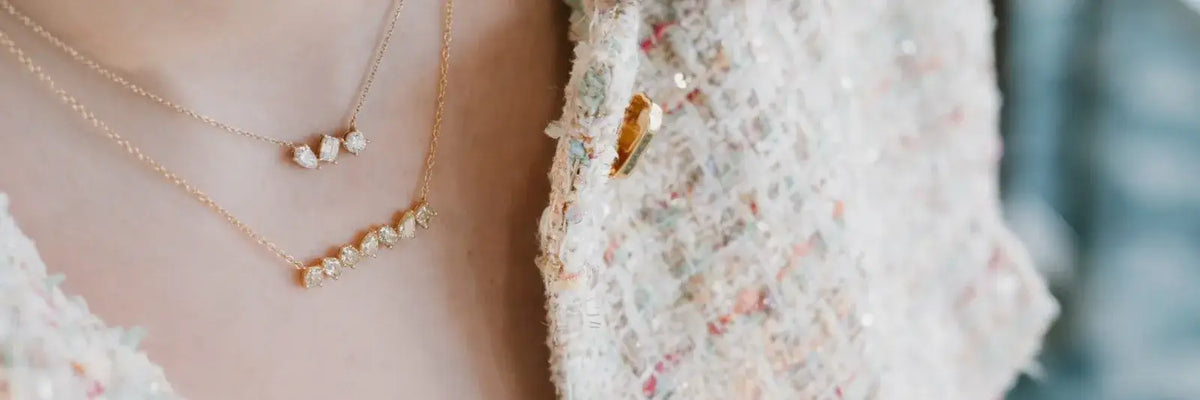 Close-up of a person wearing layered gold necklaces with small pearl-like beads, paired with a textured tweed jacket.